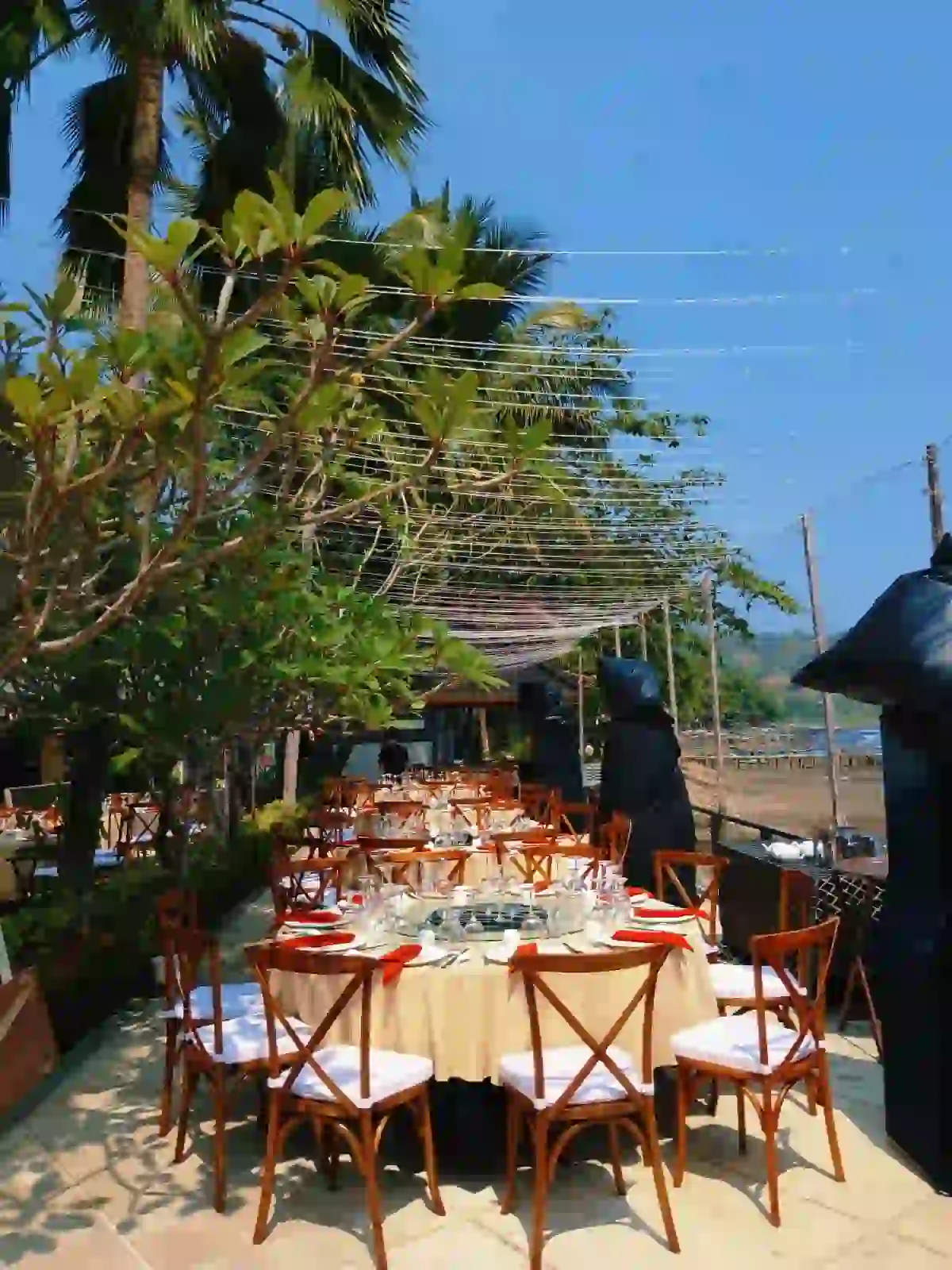 Set meja makan dengan kursi crossback kayu bantalan putih dan glassware di pinggir pantai oleh Eventara Indonesia
