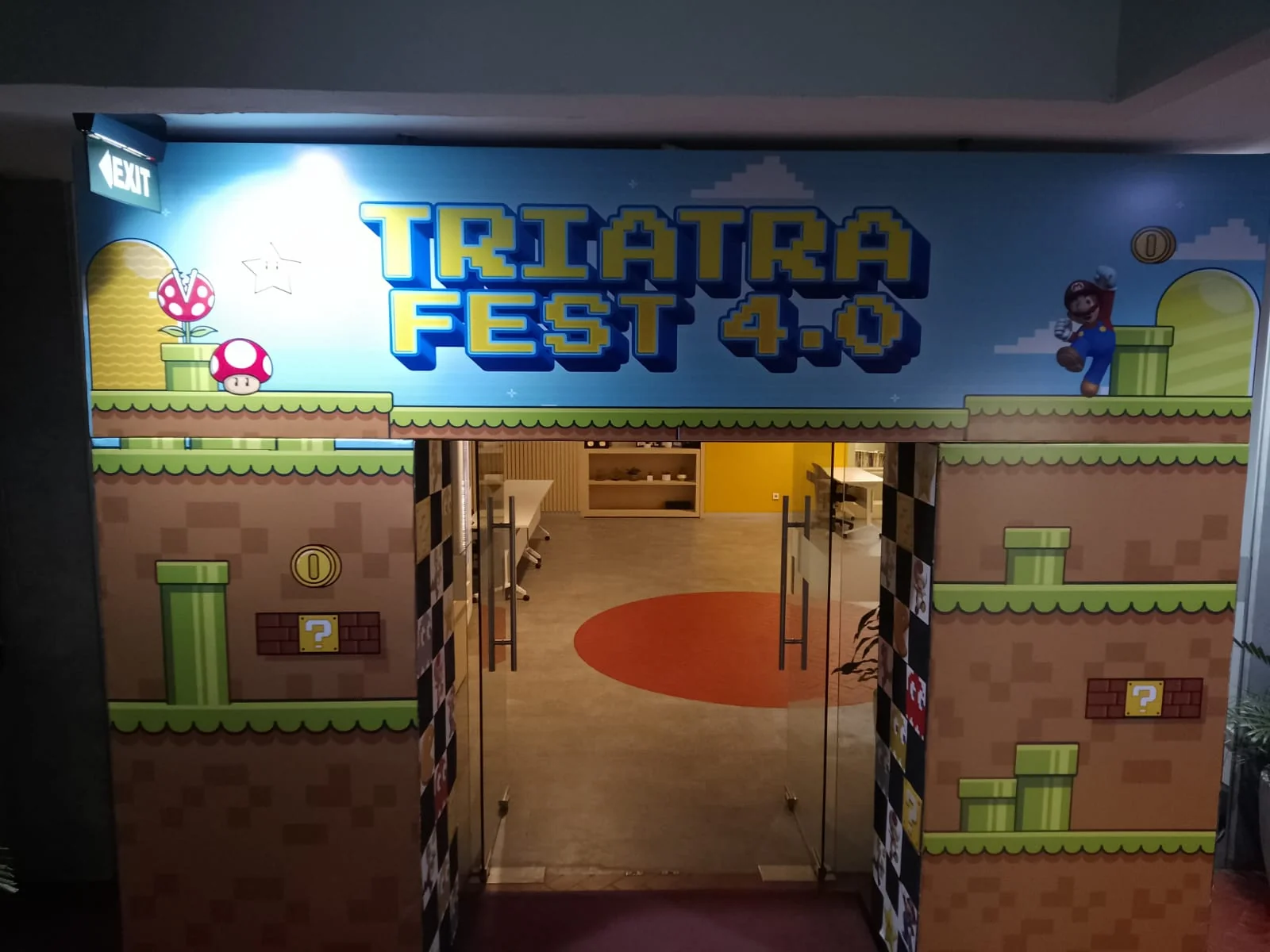 Tampak depan main entrance Triatra Fest 4.0 dengan logo acara dan visual dunia permainan retro