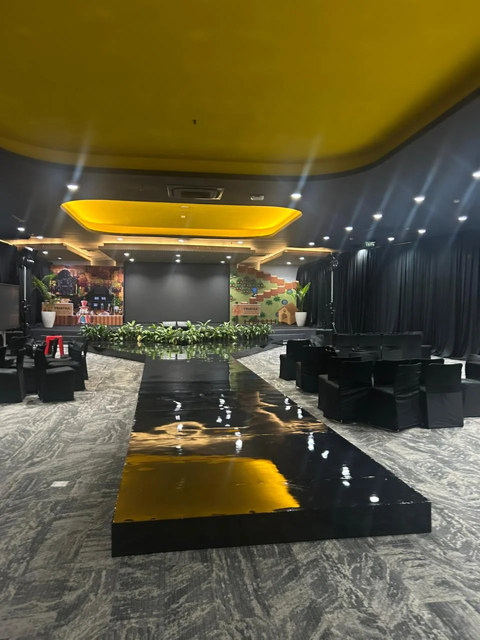 Runway menuju panggung Triatra Fest dengan seating simetris, pencahayaan ballroom dan dekorasi gaming