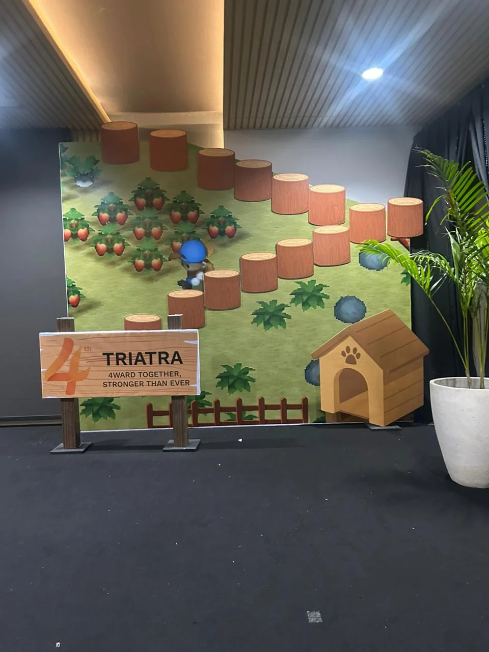 Themed activation corner Triatra Fest dengan dekorasi taman pixel art, logo acara dan elemen permainan interaktif