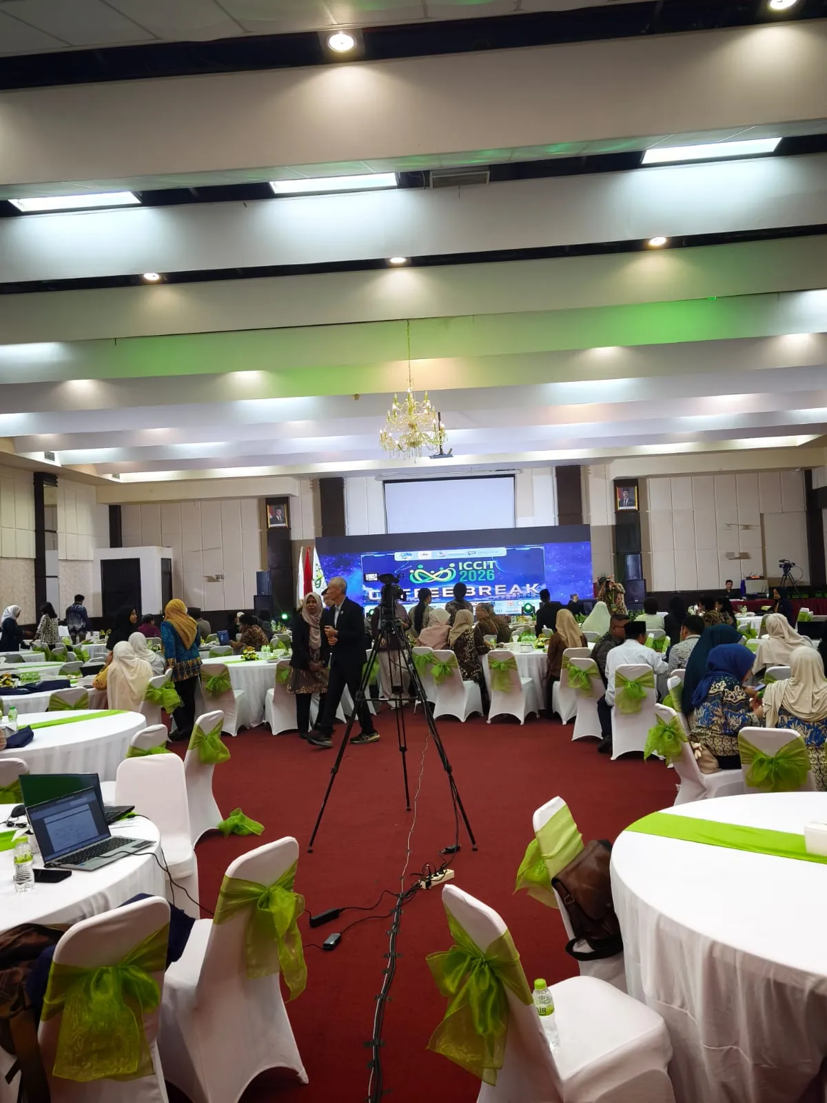 Tata ruang konferensi ICCIT 2026 di UBM dengan panggung, layar dan meja peserta