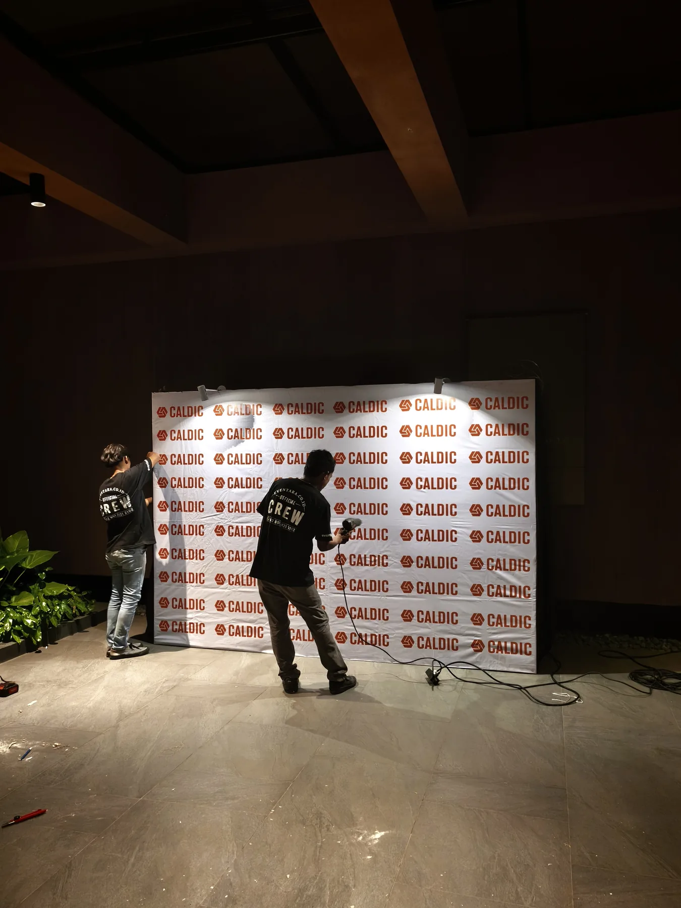 Kru memasang backdrop bermerek Caldic untuk area foto gala dinner
