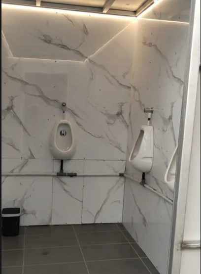 Dua urinoir porselen pria terpasang pada ruang toilet dengan lantai keramik